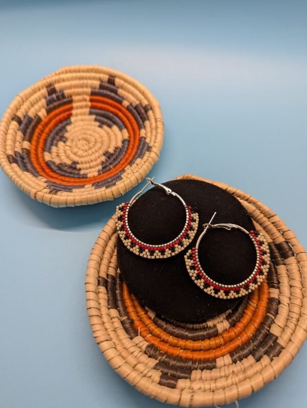 Mesa Steps Hoop Earrings By Adakair, Featuring A Striking Geometric Pattern Of Cream, Black, And Red Beads. The Earrings Are Shown On A Display Stand With A Woven Basket In The Background.